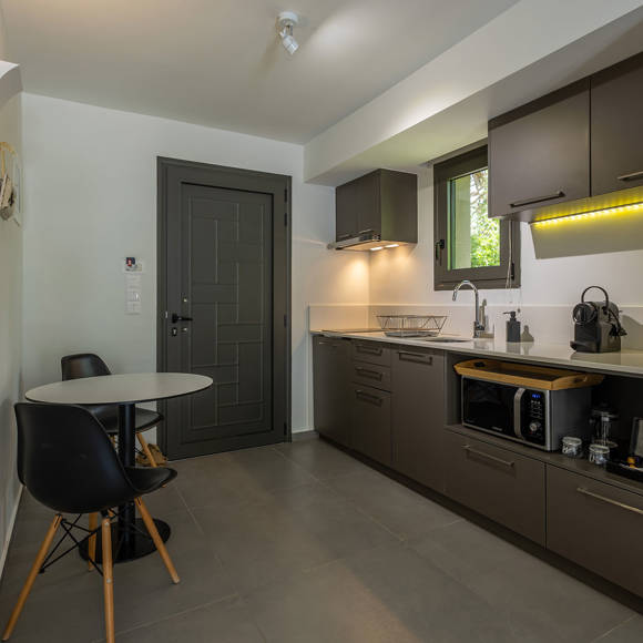 Suite's modern kitchen with dining area, dark cabinets, window and various appliances at Avdou Collection Crete