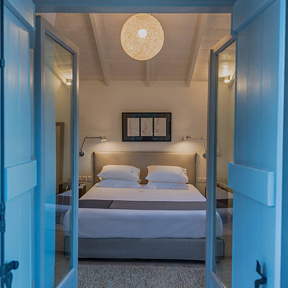 Junior villa bedroom with double bed, bedside lamps, framed artwork and warm ceiling light at Avdou Collection