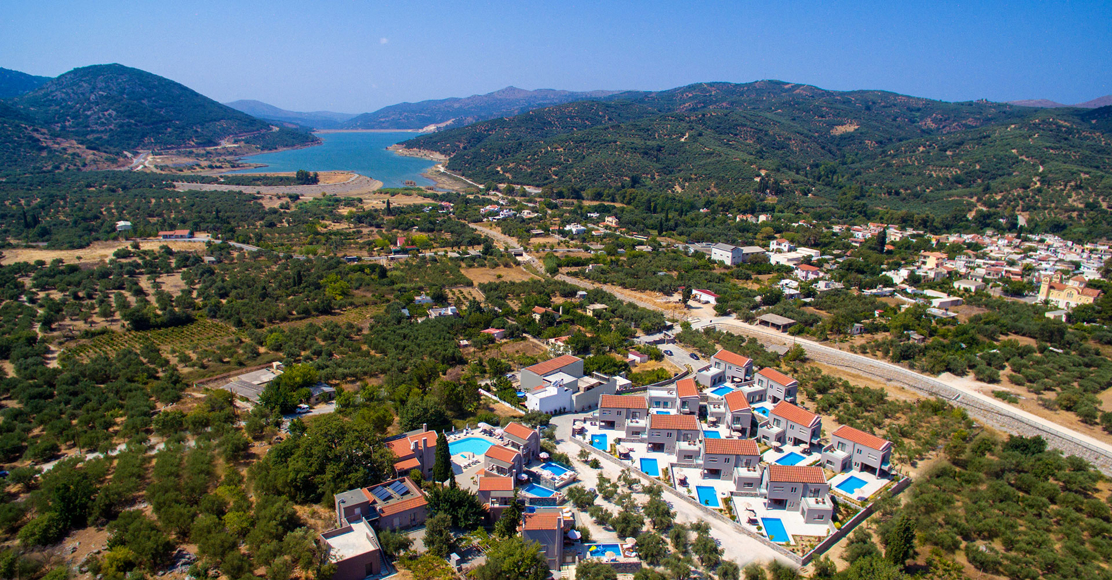 Aerial view of Avdou Collection surrounded by olive groves and mountains near the scenic lake in Crete