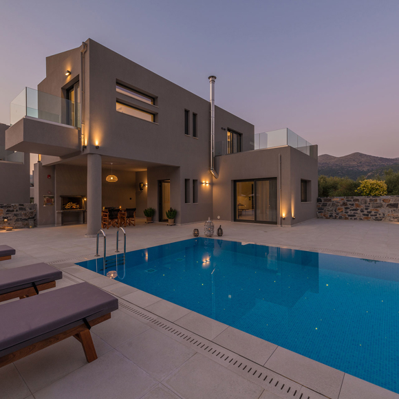 Grand villa private pool area with sunbeds, evening lights and mountain backdrop in luxury setting at Avdou Collection