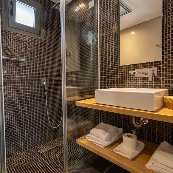Suite's modern bathroom with walk in shower, wooden vanity and dark tiles at Avdou Collection Crete