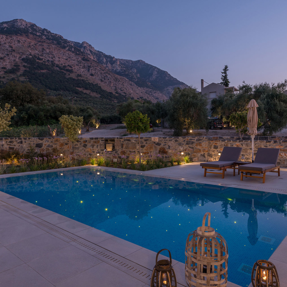 Grand villa with two bedrooms featuring an illuminated pool and mountain views in the evening at Avdou Collection