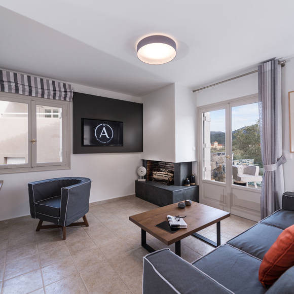 Junior villa living room with grey sofa, fireplace, TV and terrace access with mountain views at Avdou Collection
