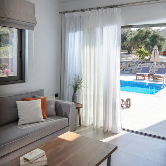 Living room with sofa, coffee table and pool view through glass doors in the two bedroom grand villa at Avdou Collection