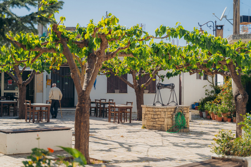 Avdou village in Crete in a sunny day with trees, outdoor tables and a stone well 
