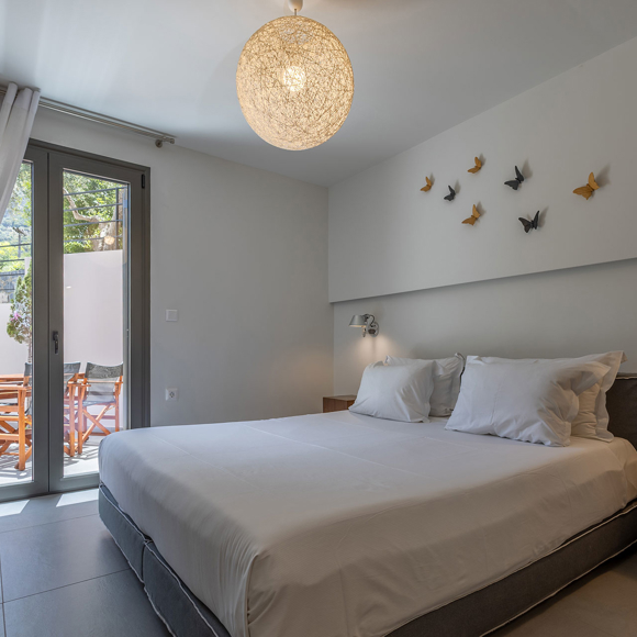 Suite's modern bedroom with double bed and balcony door, minimalist decor and bedside table at Avdou Collection