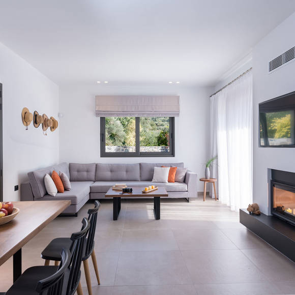 Spacious living room with corner sofa, fireplace, dining area and large windows in the two bedroom grand villa