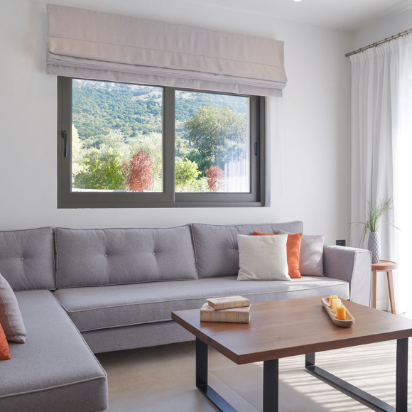 Spacious living room with corner sofa, colorful cushions and large window overlooking nature in the grand villa Avdou Collection
