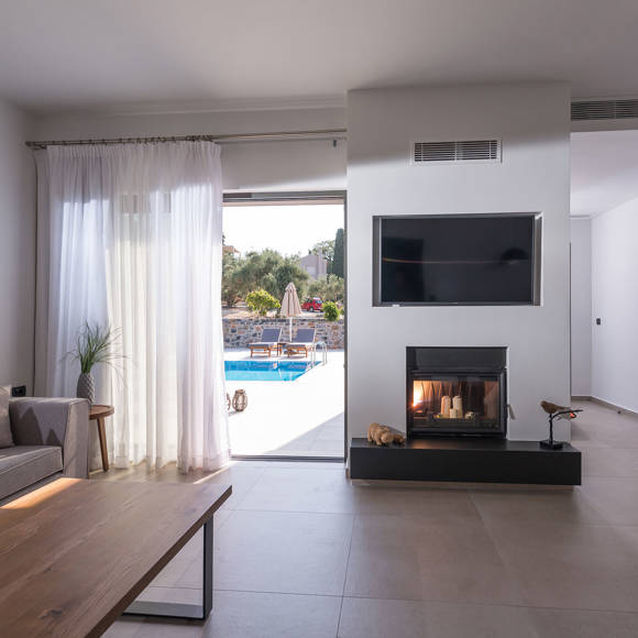 Living room with fireplace, sofa and direct access to the private pool in the two bedroom grand villa at Avdou Collection