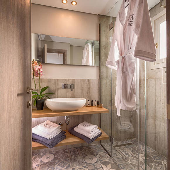 Junior villa's modern bathroom with wooden vanity, vessel sink, patterned tiles and glass shower at Avdou Collection