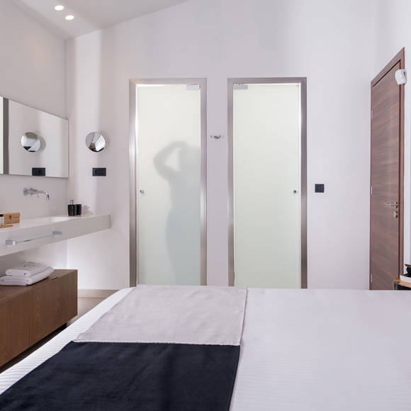 Modern master bedroom with ensuite bathroom, large mirror and elegant minimalist design in the two bedroom grand villa Avdou Collection