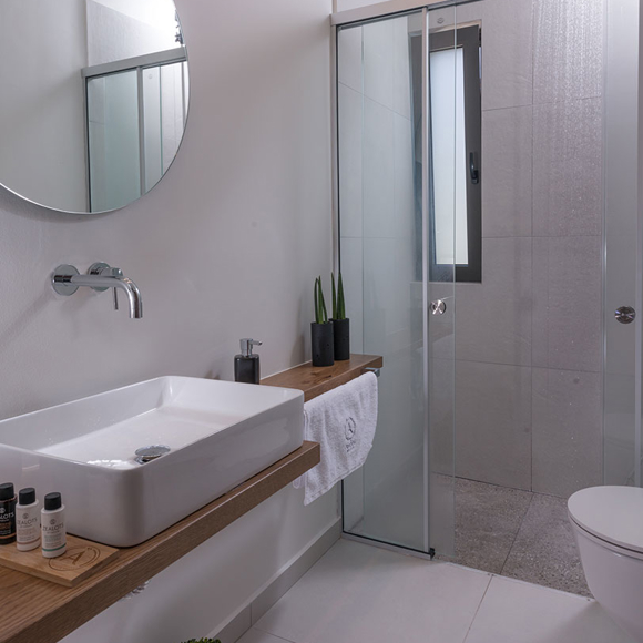 Elegant bathroom featuring a glass walk in shower, round mirror, modern sink and natural wood accents 