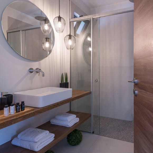 Grand villa bathroom with round mirror, glass shower, hanging lights and wooden vanity at Avdou Collection