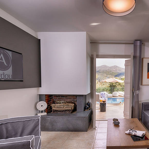 Junior villa living room with fireplace, flat screen TV, sofa with orange pillows and pool view at Avdou Collection