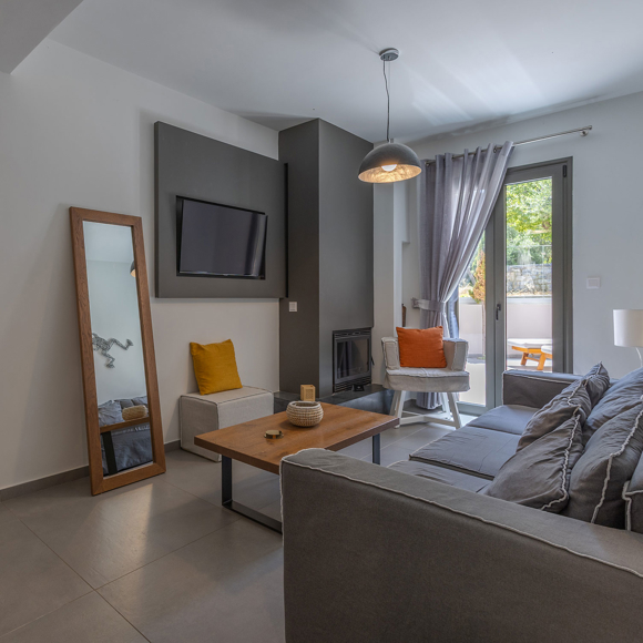 Suite's living room with sofa, fireplace and large mirror, decorated with neutral tones at Avdou Collection