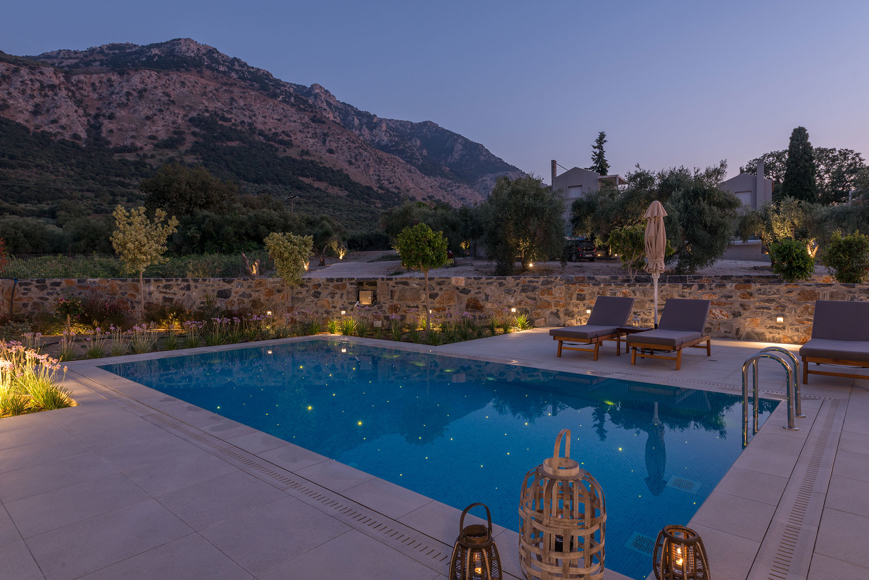 Grand villa pool with lanterns, sunbeds and evening mountain views in serene atmosphere at Avdou Collection