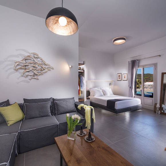 Open plan suite with living area, and bedroom featuring a gray sofa, wooden table and view at Avdou Collection